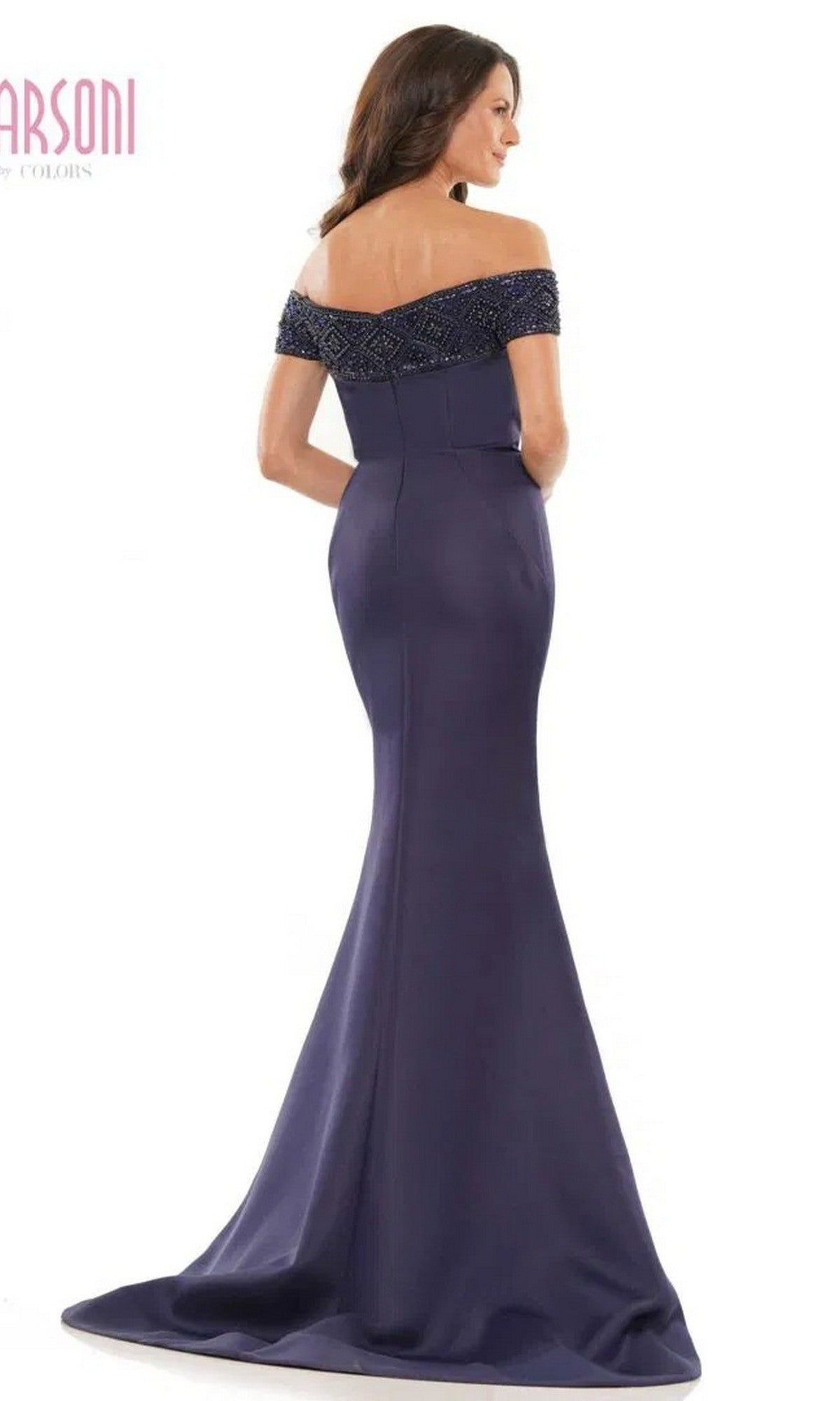 A woman faces away from the camera in the Marsoni MV1184, a long formal dress featuring an off-the-shoulder navy blue design, fitted bodice with beaded details, and an elegant floor-length mermaid skirt.